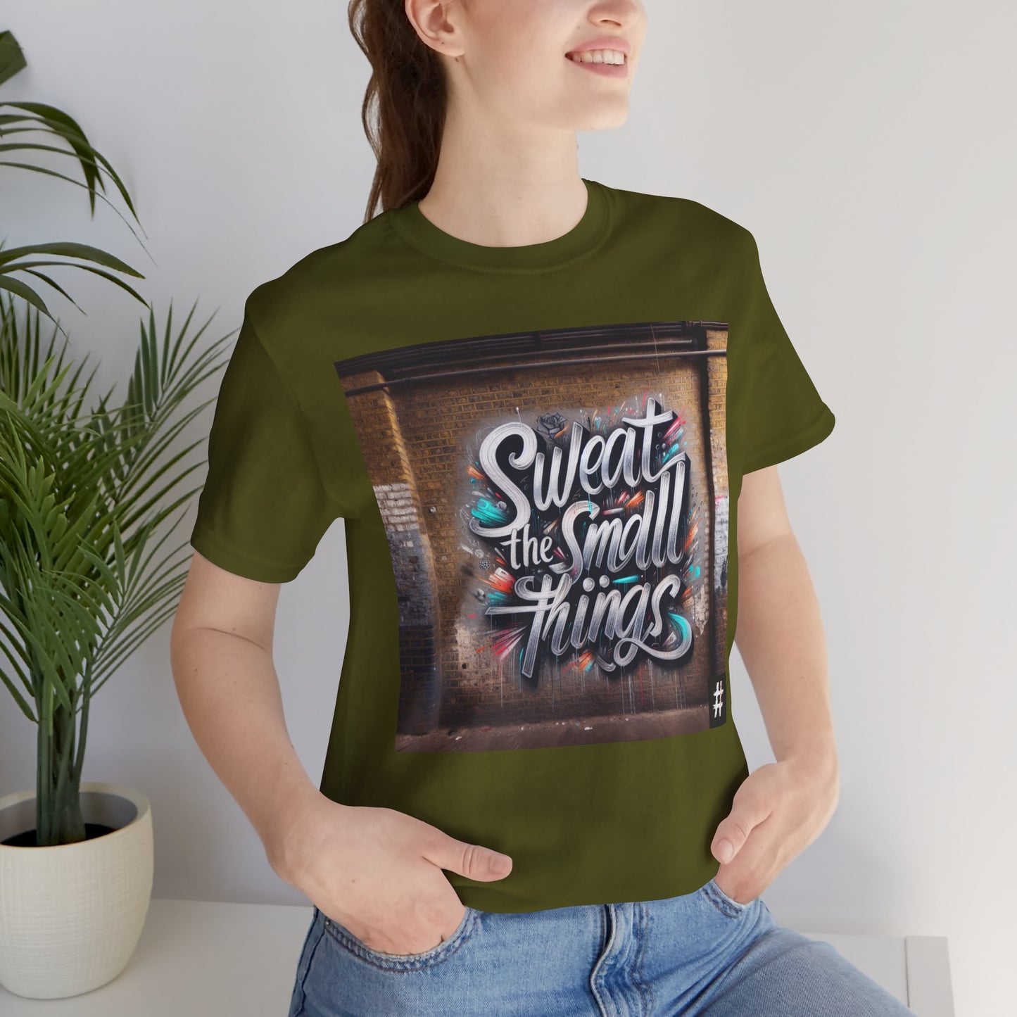 A woman wearing w olive green Unisex ‘Sweat the Small Things’ graphic tee — bold typography shirt highlighting that small details and daily discipline create the foundation for every big achievement.