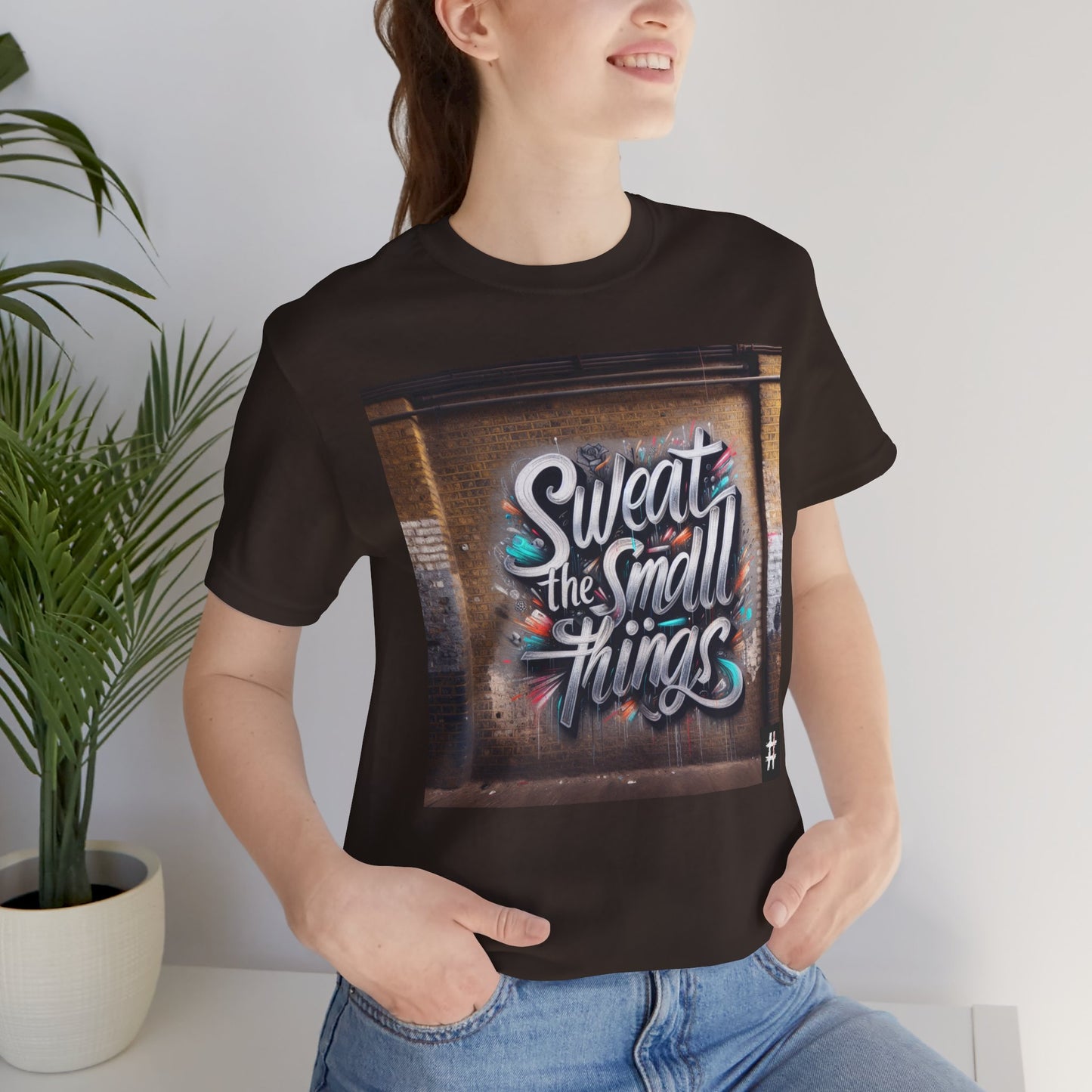 A woman wearing a dark brown Unisex ‘Sweat the Small Things’ graphic tee — bold typography shirt highlighting that small details and daily discipline create the foundation for every big achievement.